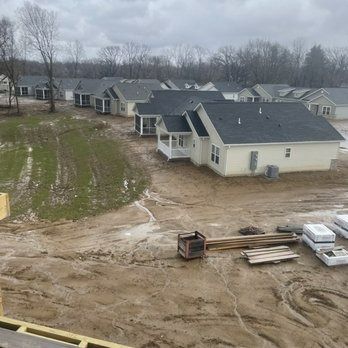 Person in grey shirt and gloves painting a light-colored section on brown siding with a brush.