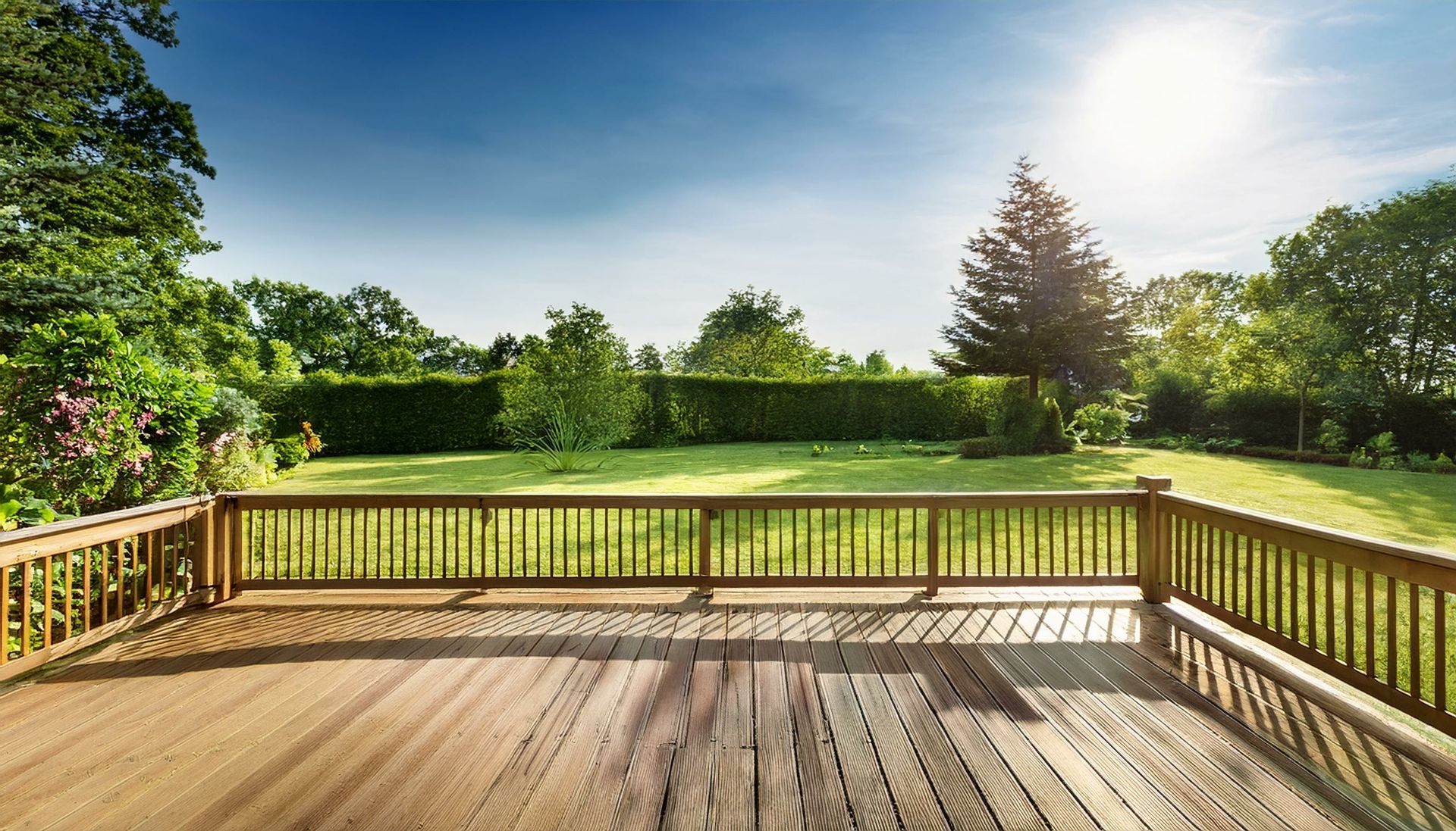 An empty wooden deck with a wooden railing overlooking a lush green garden.