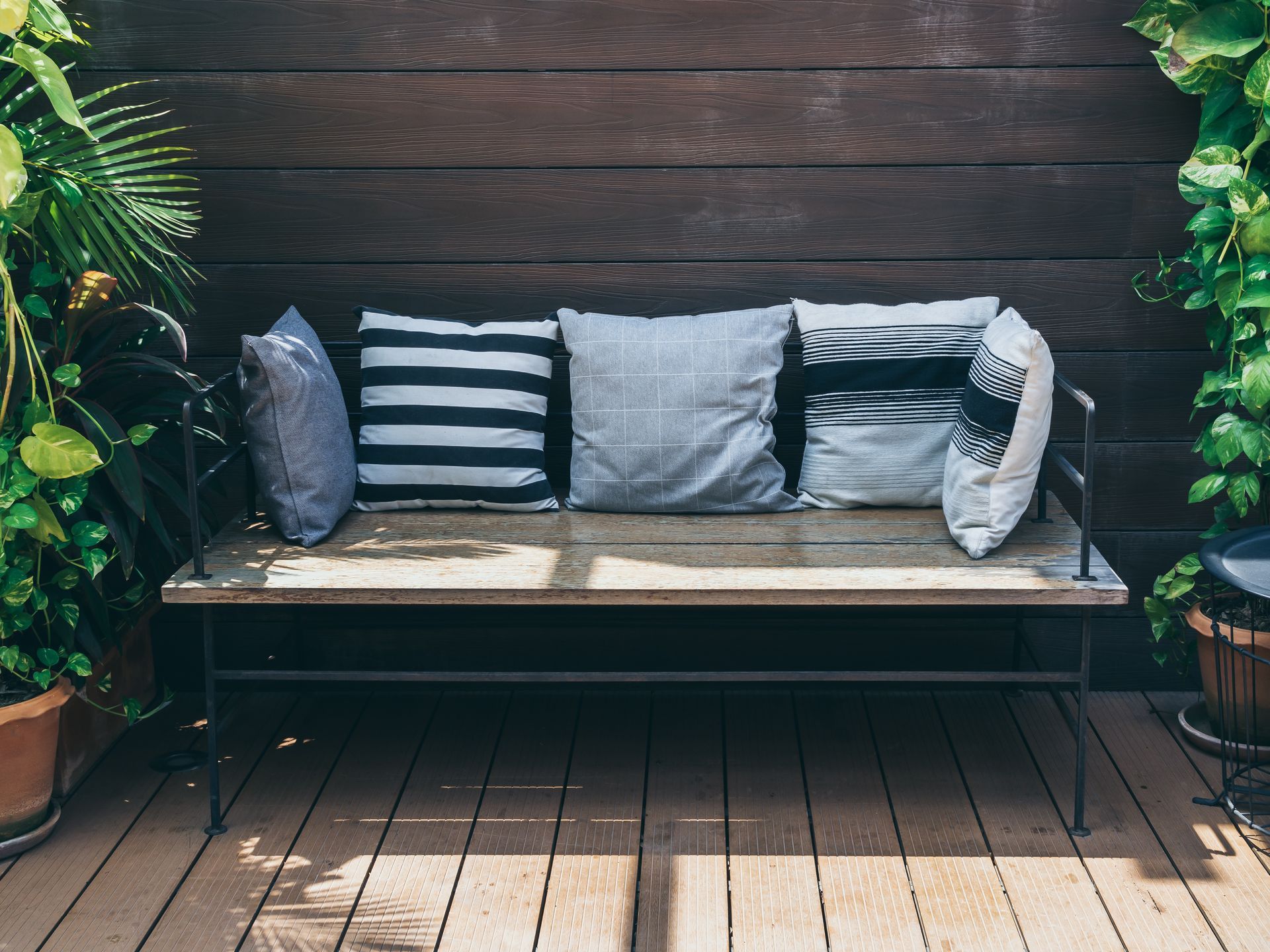 A wooden bench with pillows on it is sitting on a wooden deck.