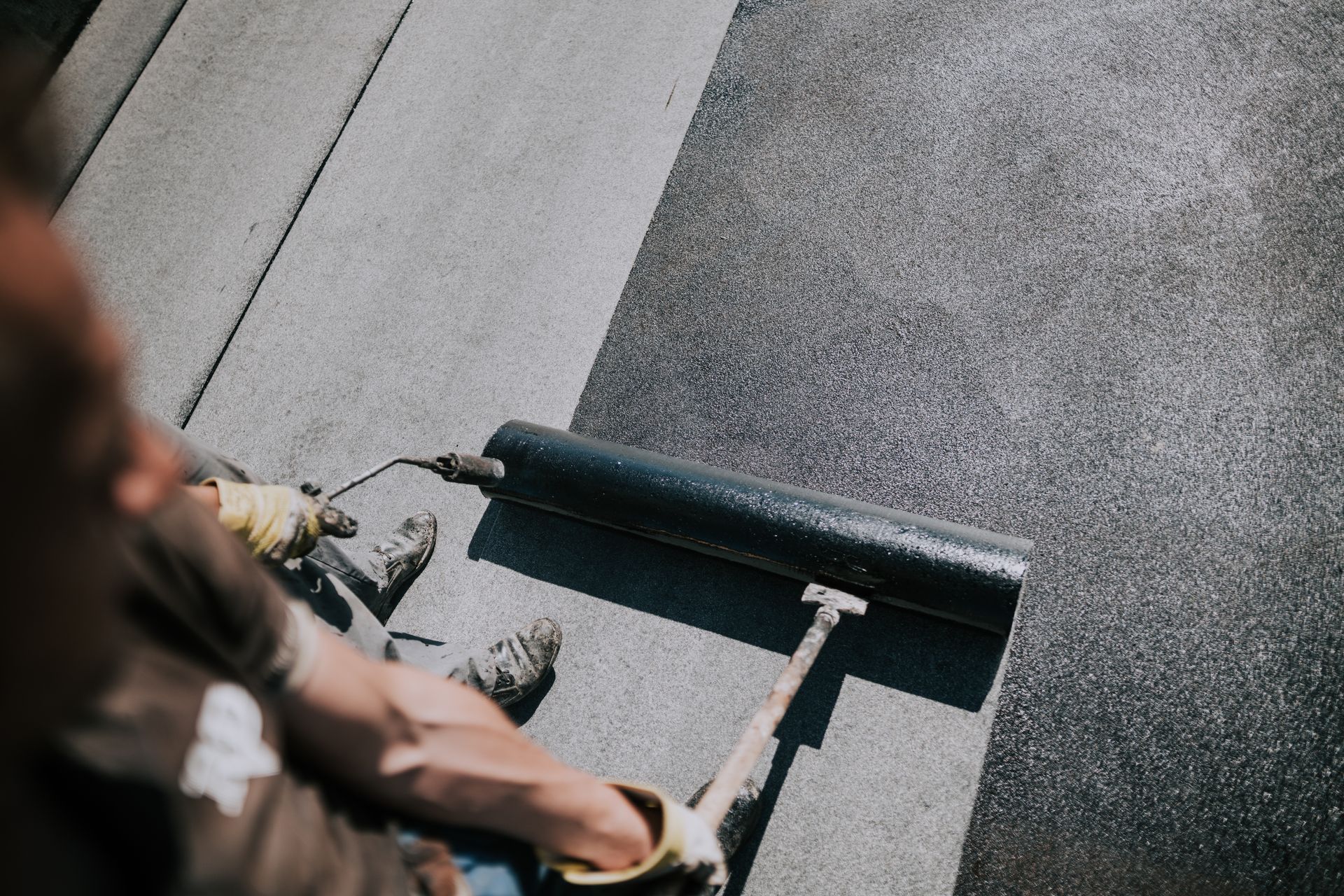 A man is laying a roll of asphalt on a roof.