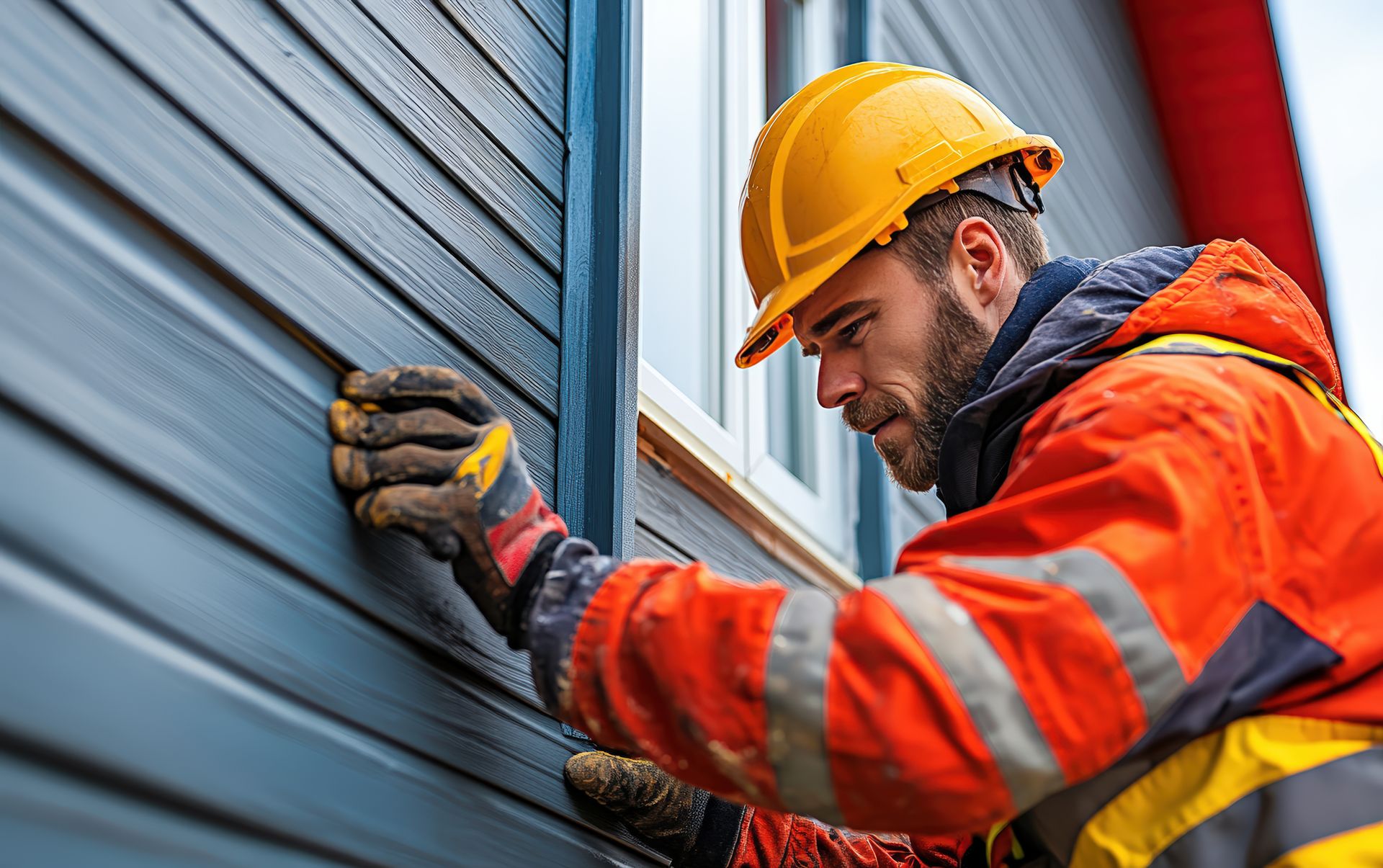 A man wearing a hard hat and gloves is working on a building.