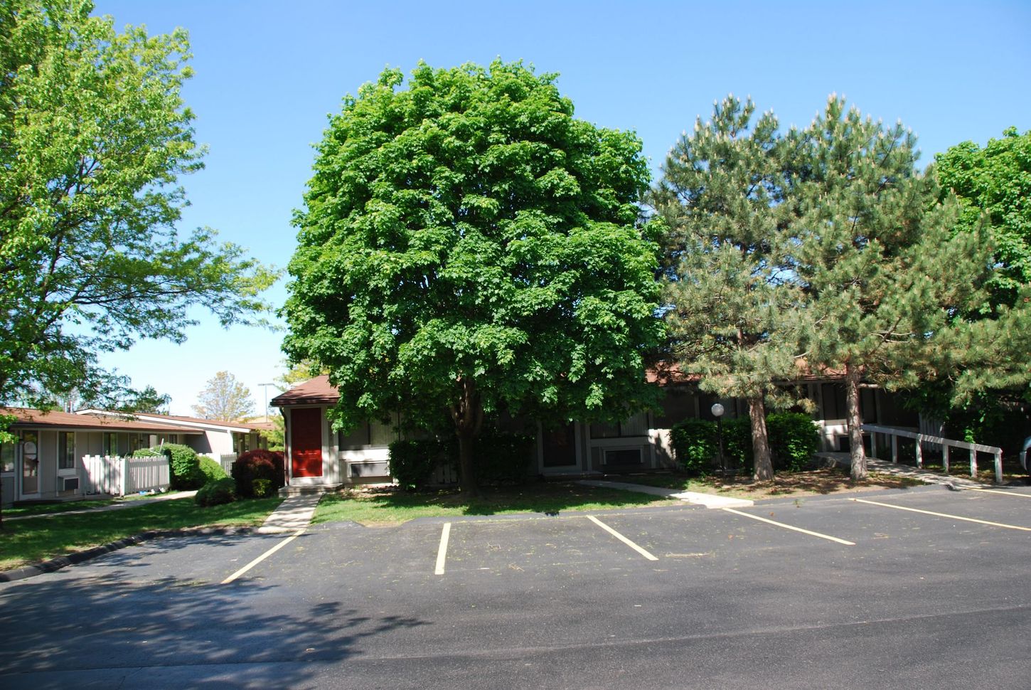 A parking lot in front of a house with trees in the background