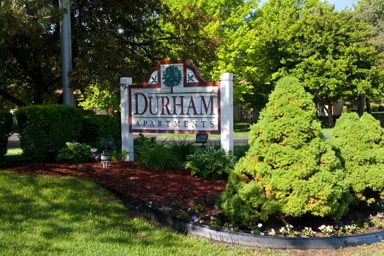 A sign for durham apartments is surrounded by trees and bushes