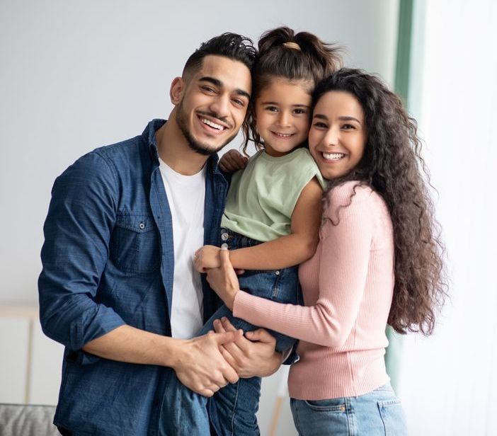 A man and woman are holding a little girl in their arms.