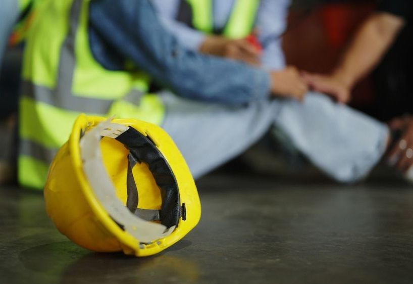 A construction worker is sitting on the floor with a hard hat on the ground.