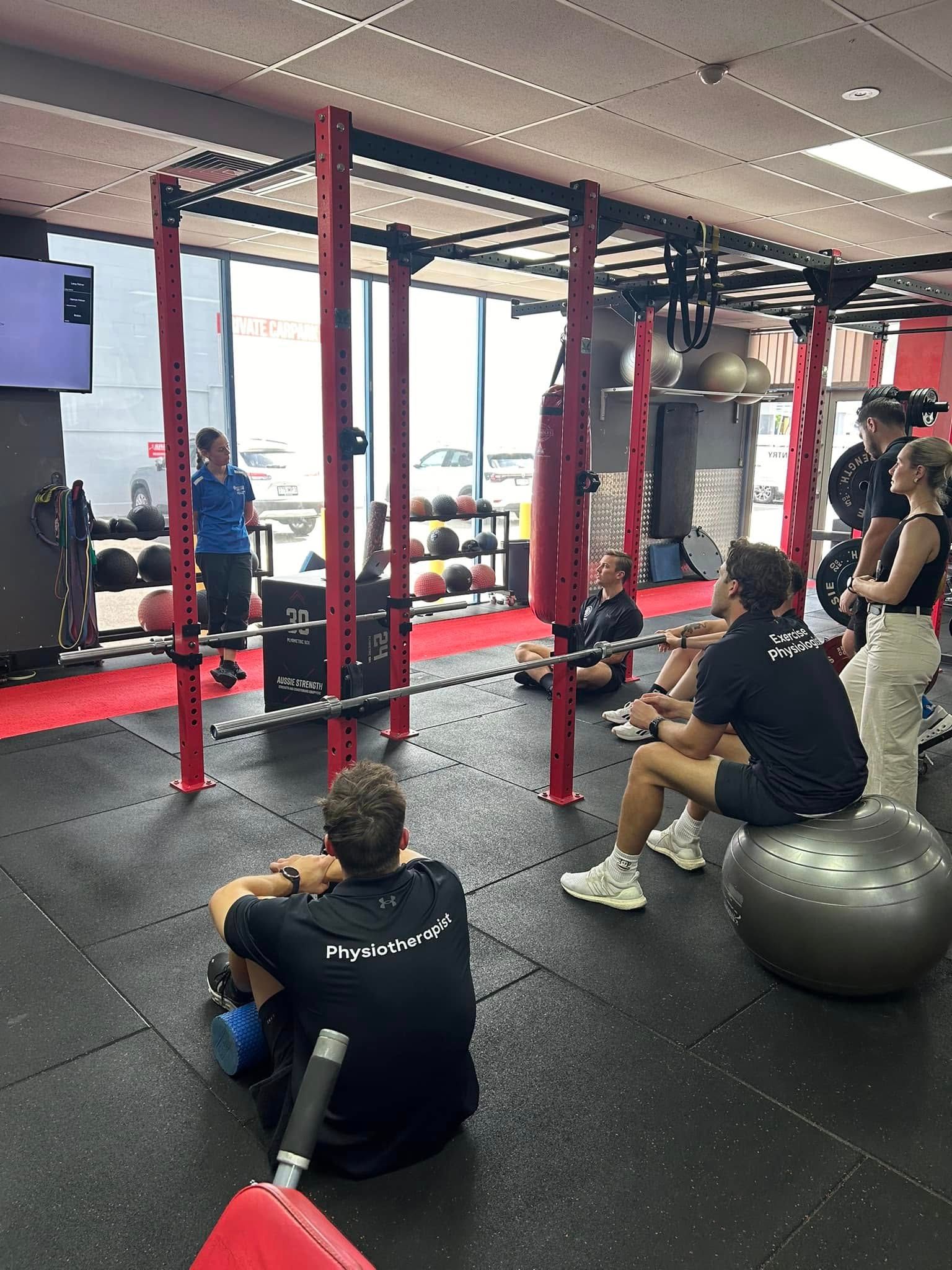 A Group Of People Are Sitting On The Floor In A Gym – Health First Townsville In Townsville, QLD
