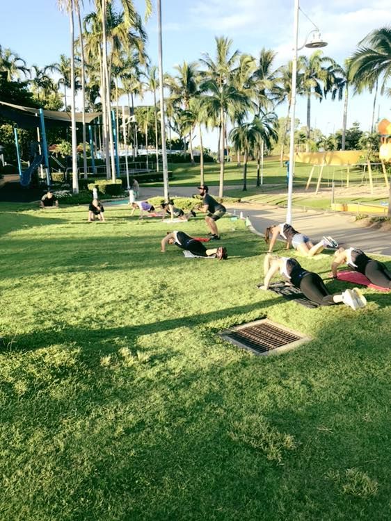 A Group of People Are Doing Push Ups on the Grass in a Park — Health First Townsville In Townsville, QLD