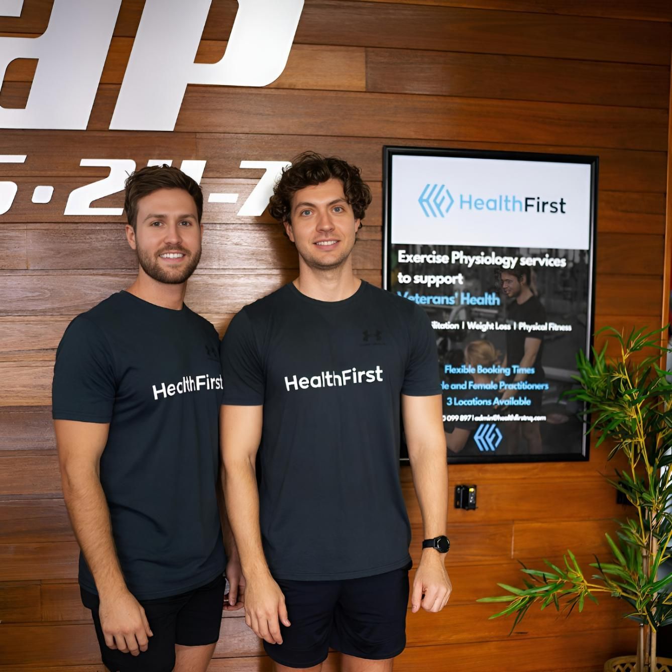 Two Men Are Standing in Front of a Sign That Says Healthfirst — Health First Townsville in Townsville, QLD