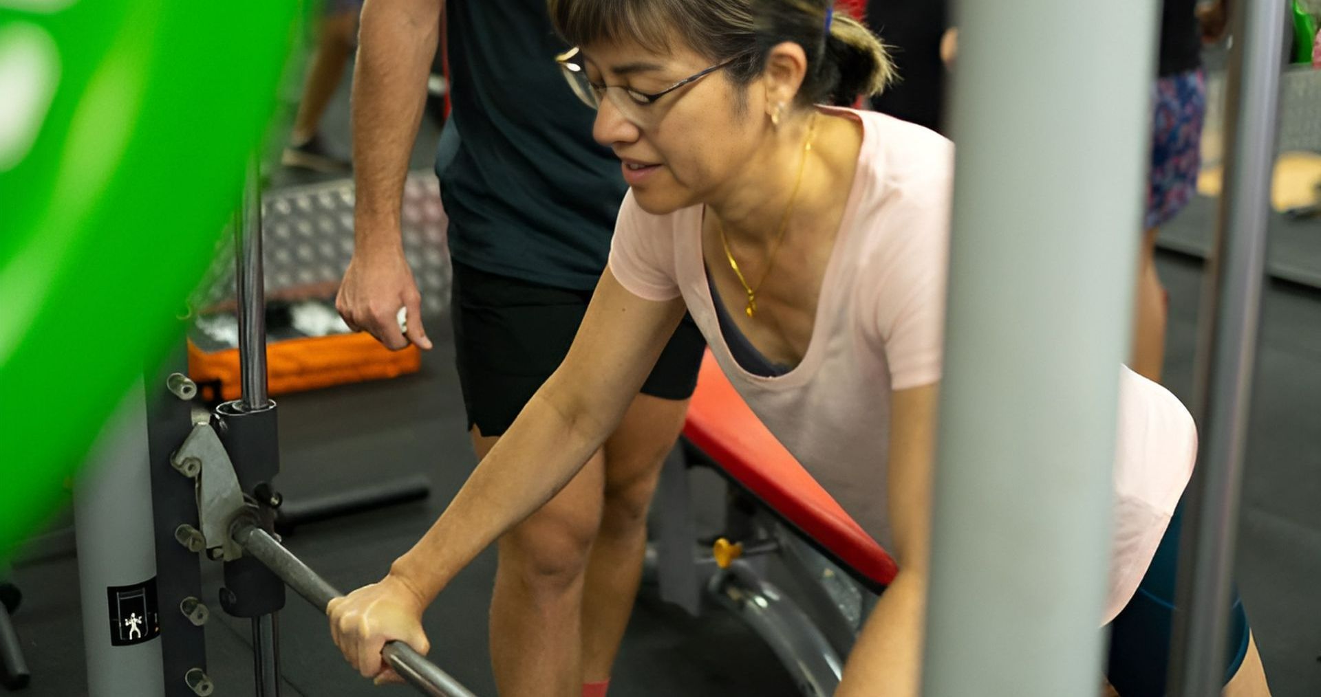 A Man is Helping a Woman Lift a Barbell in a Gym β Health First Townsville In Townsville, QLD