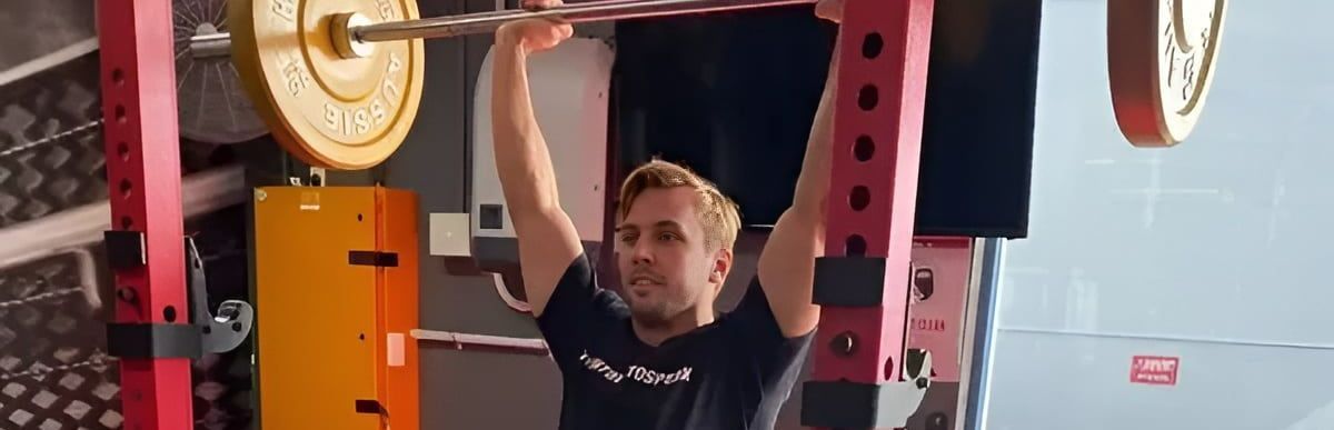 A Man is Lifting a Barbell Over His Head in a Gym — Health First Townsville In Thuringowa, QLD