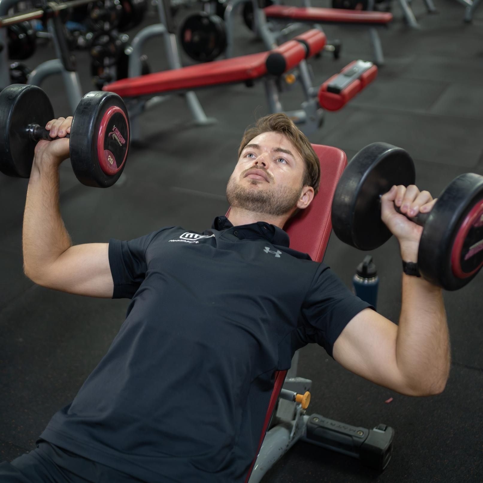 A Man in a Black Shirt is Lifting Dumbbells in a Gym — Health First Townsville In Townsville, QLD