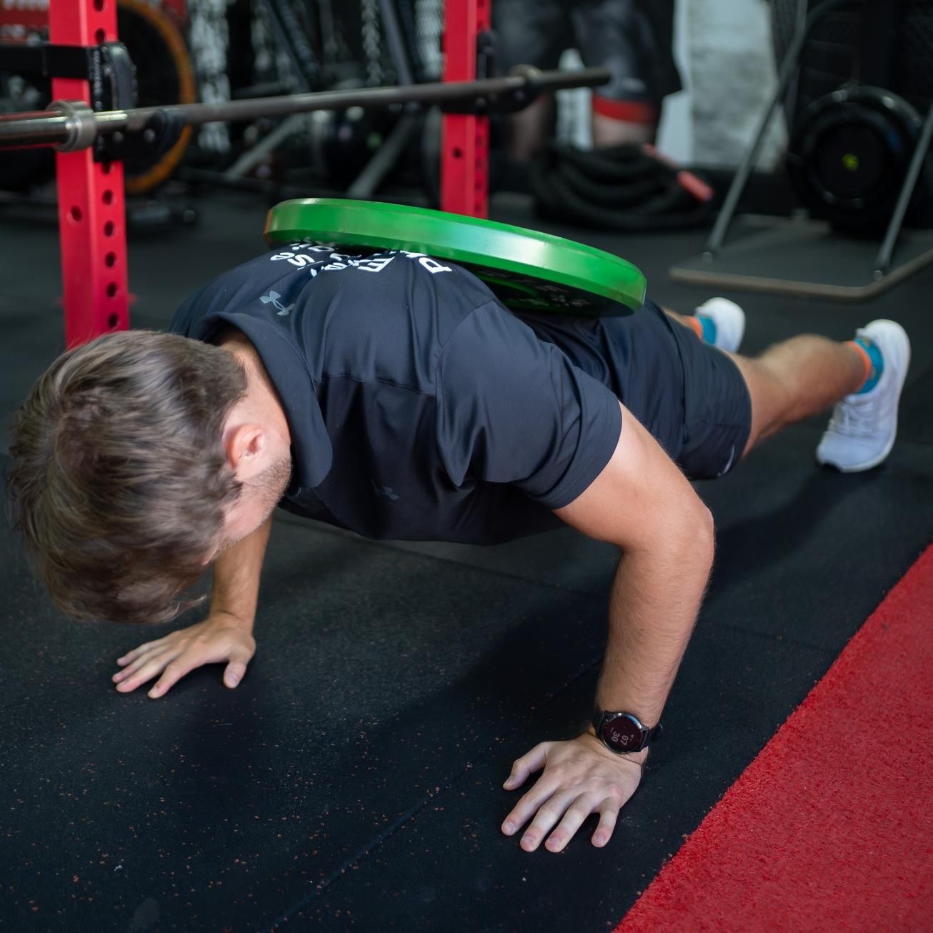 A Man is Doing Push Ups With a Green Plate on His Back — Health First Townsville In Townsville, QLD