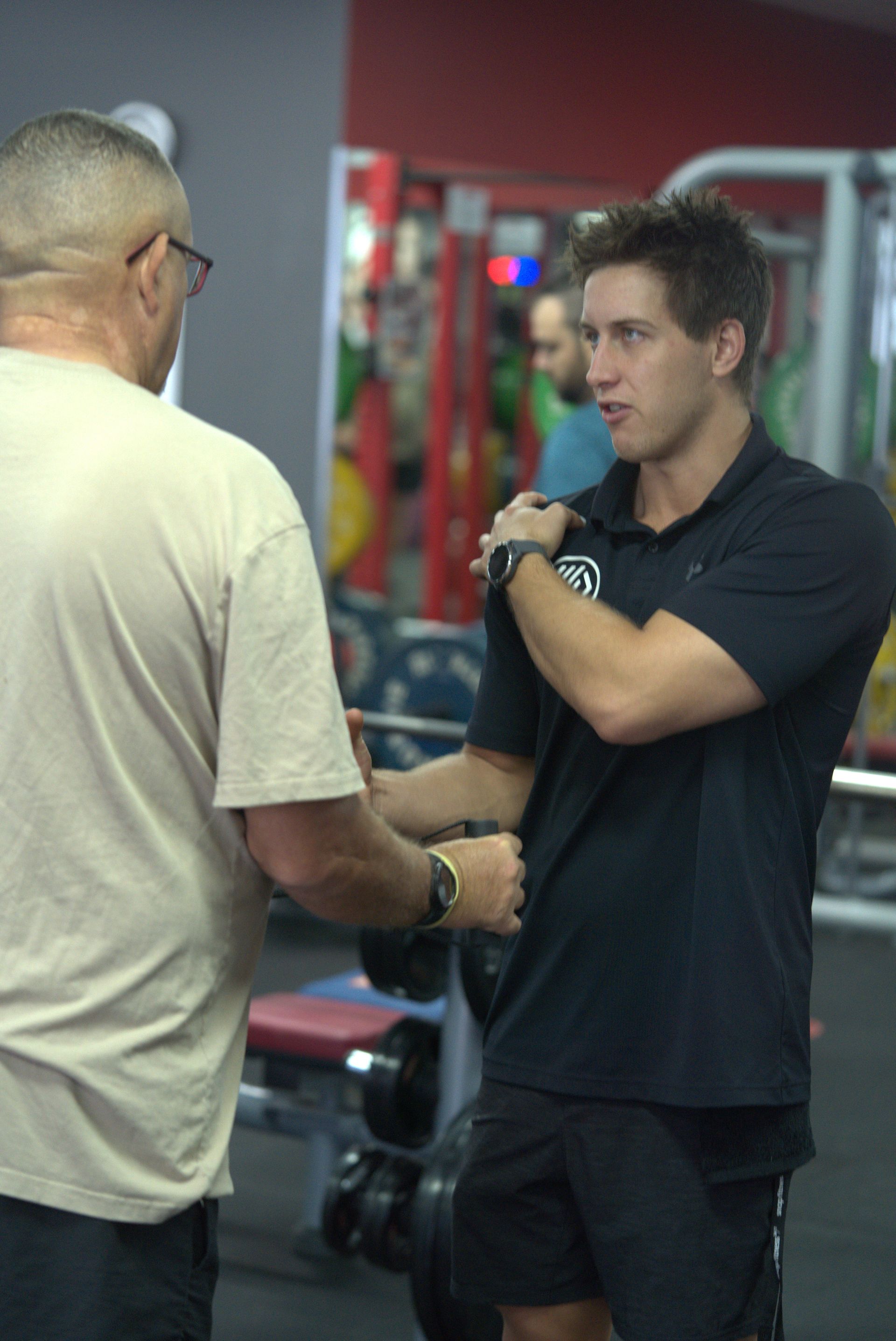 A Man Wearing Glasses is Helping Another Man With His Arm — Health First Townsville In Townsville, QLD