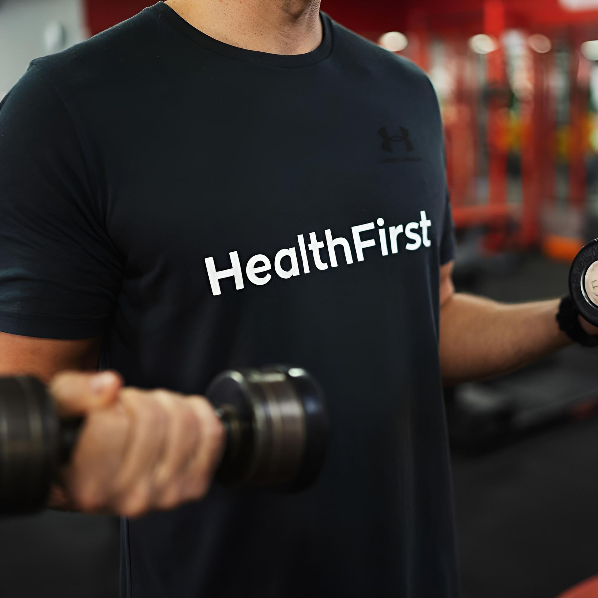 A Man Wearing a Health First Shirt is Lifting Dumbbells — Health First Townsville In Townsville, QLD