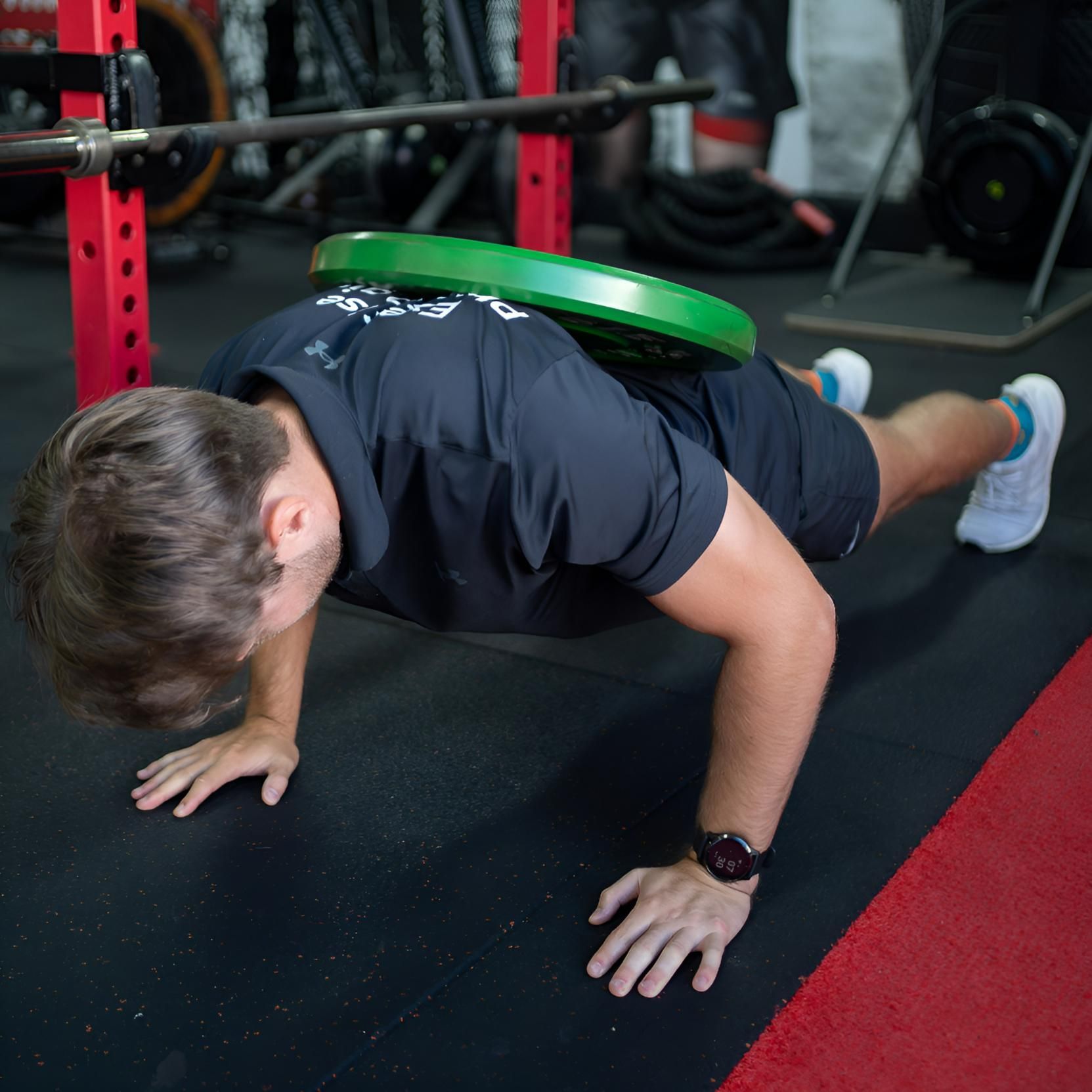 A Man is Doing Push Ups With a Green Plate on His Back β Health First Townsville In Townsville, QLD