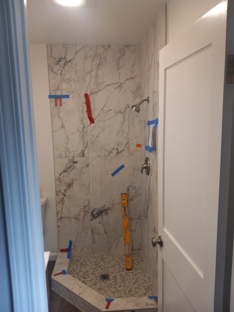 A shower is being remodeled in a bathroom with marble tiles and a level.