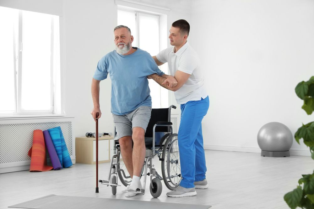A Man in a Wheelchair is Being Helped by a Nurse to Walk — AMC Exercise Physiology in Maitland, NSW