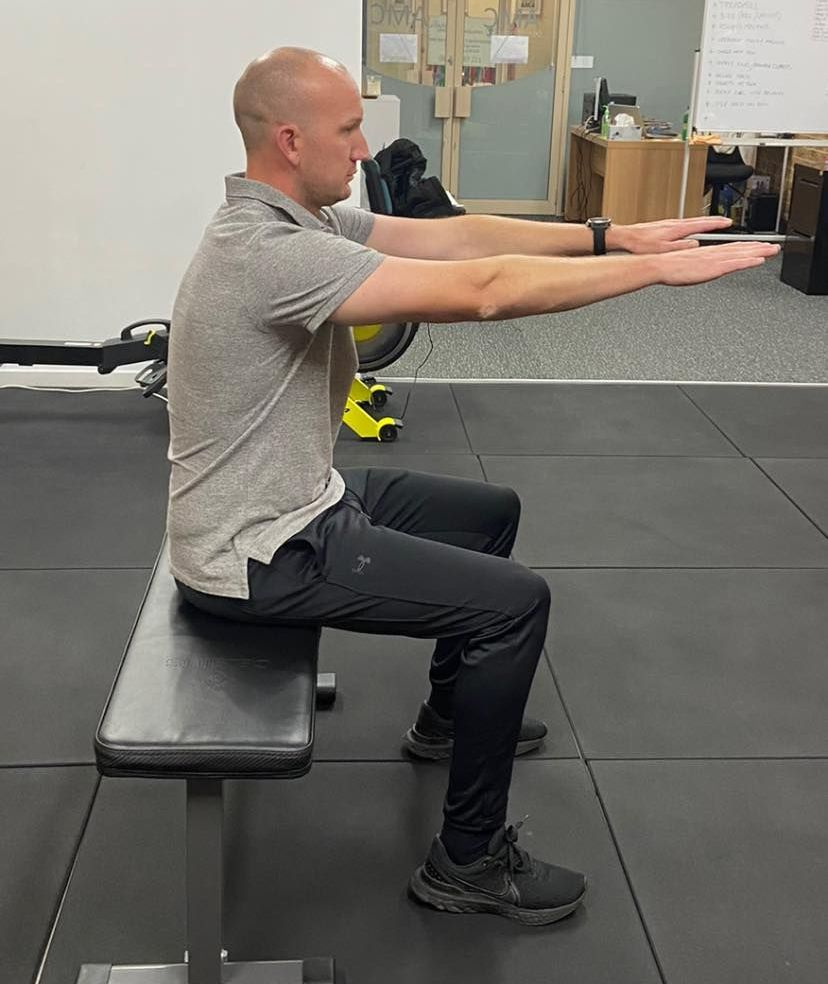 A Man is Sitting on a Bench in a Gym With His Arms Outstretched — AMC Exercise Physiology in Maitland, NSW