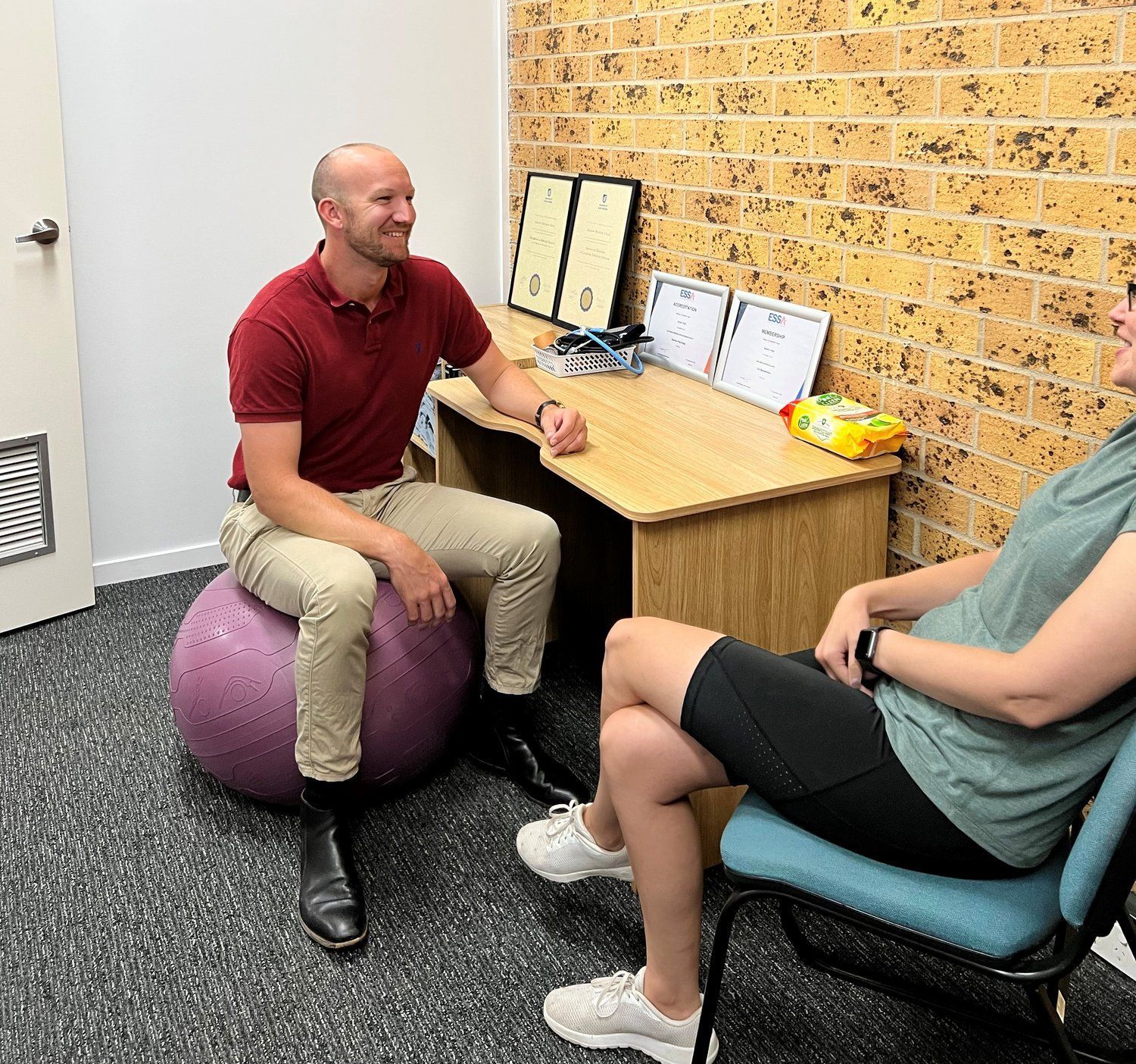 A man is sitting on a purple ball talking to a pregnant woman — AMC Exercise Physiology in Maitland, NSW