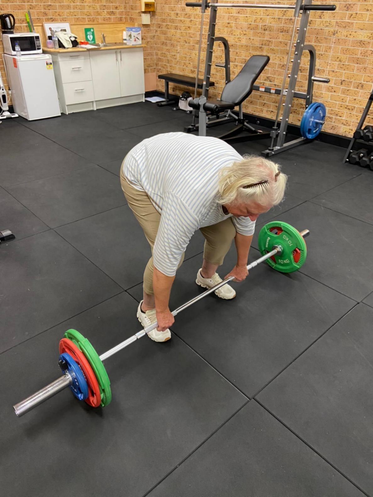 A Woman Is Lifting a Barbell in A Gym — AMC Exercise Physiology in Maitland, NSW