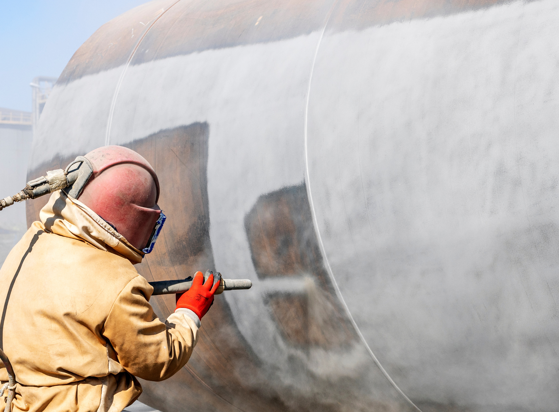 a man wearing a helmet and gloves is sandblasting a wall .