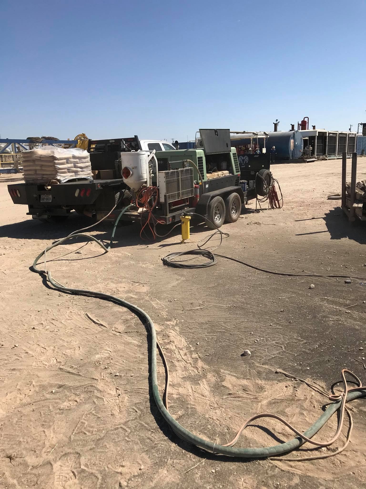 a truck with a hose attached to it is parked in a dirt field .