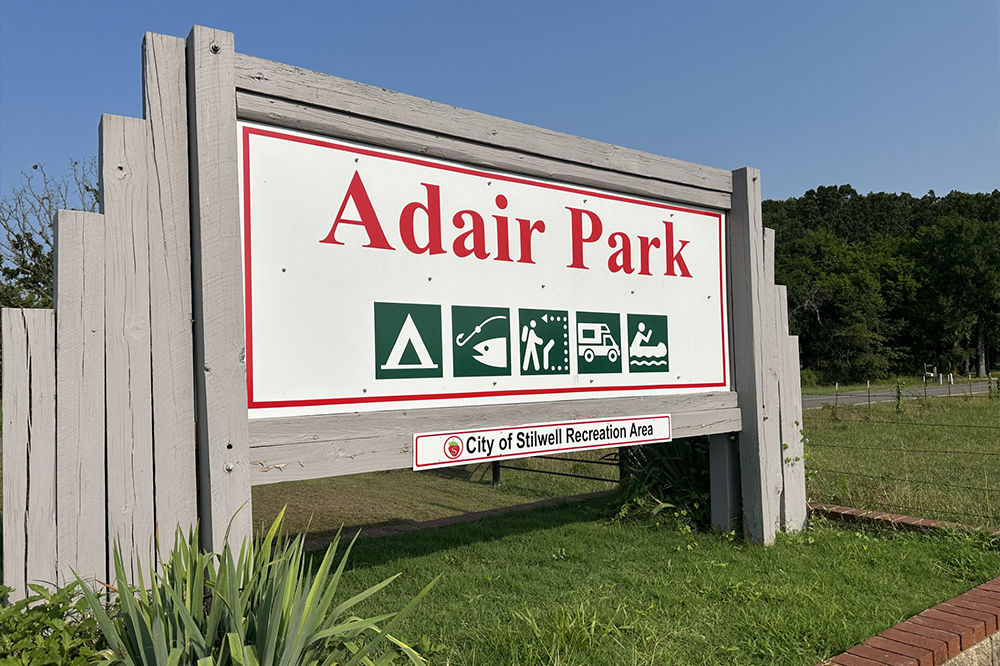 A sign for adair park is hanging over a grassy field.