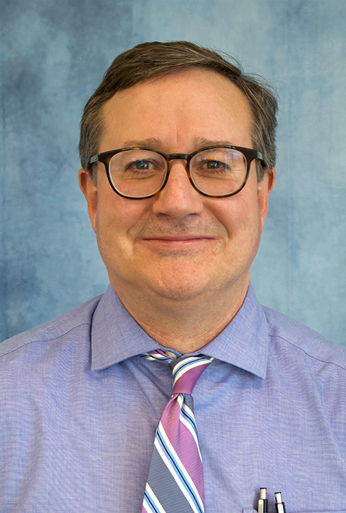A man in a purple shirt and tie is smiling for the camera.