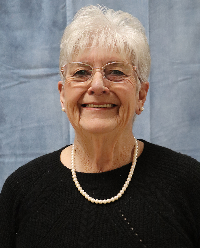 An older woman wearing glasses and a pearl necklace is smiling for the camera.