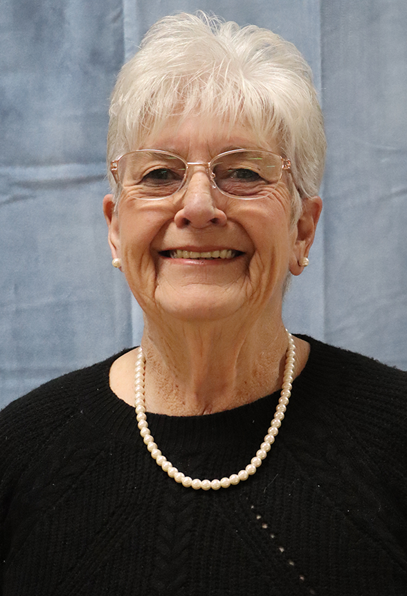 An older woman wearing glasses and a pearl necklace is smiling for the camera.