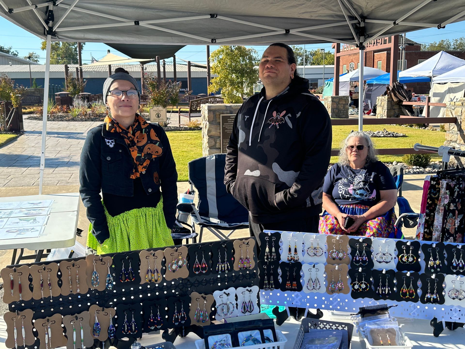 A man and a woman are standing in front of a table with earrings on it.