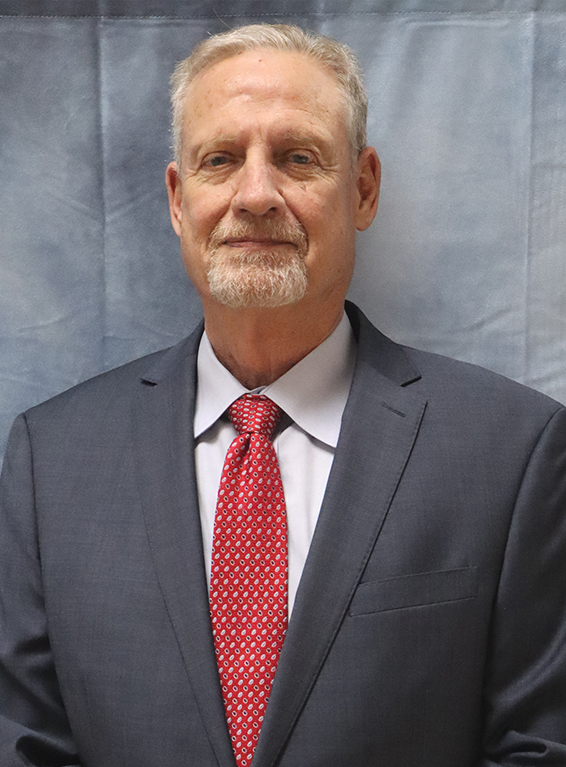 A man in a suit and tie is standing with his hands folded