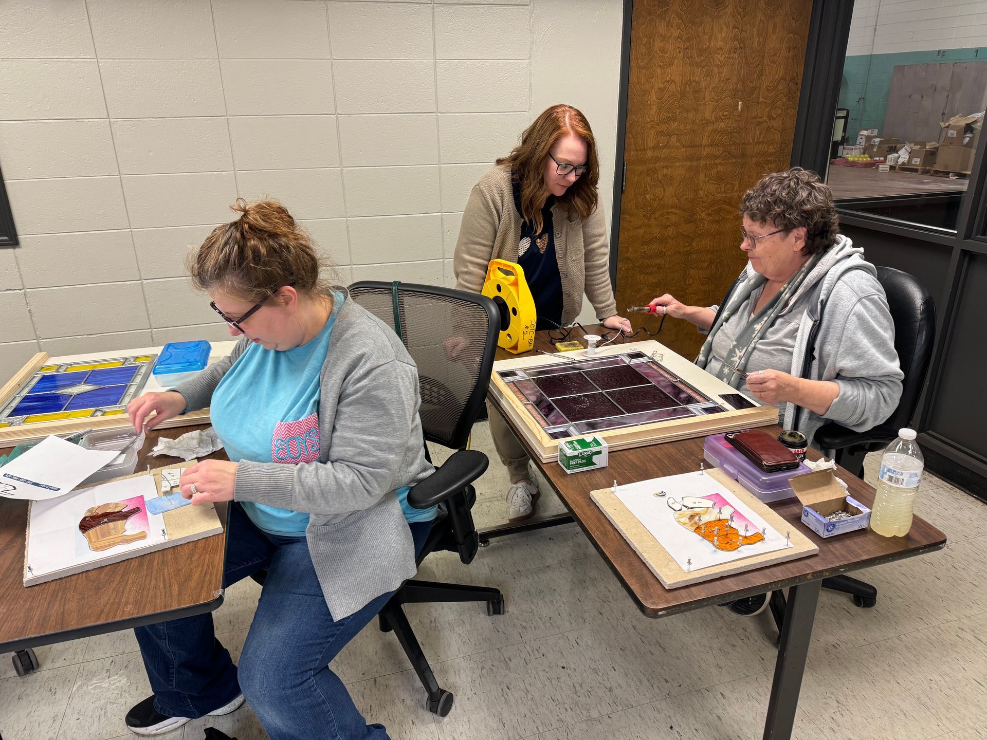 Melissa Wofford starts a small buffalo for fun. Behind her, instructor Rhonda Cravens, seated, shows Shelly Matthews how to solder holders onto her finished piece.