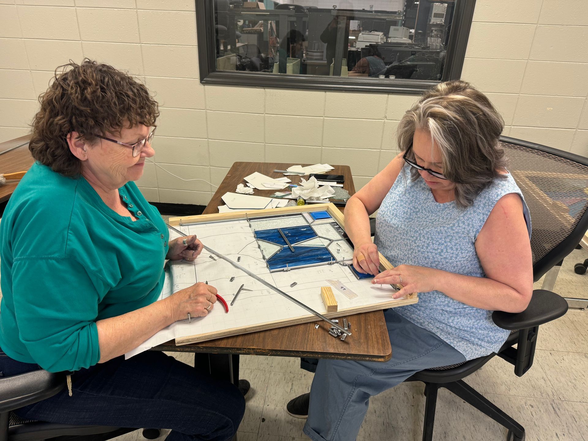 Stained glass instructor Rhonda Cravens helps Shelley Brandon fit a piece of glass and secure it with a nail.