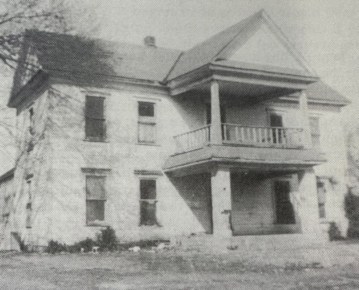 A black and white photo of an old house with a balcony.