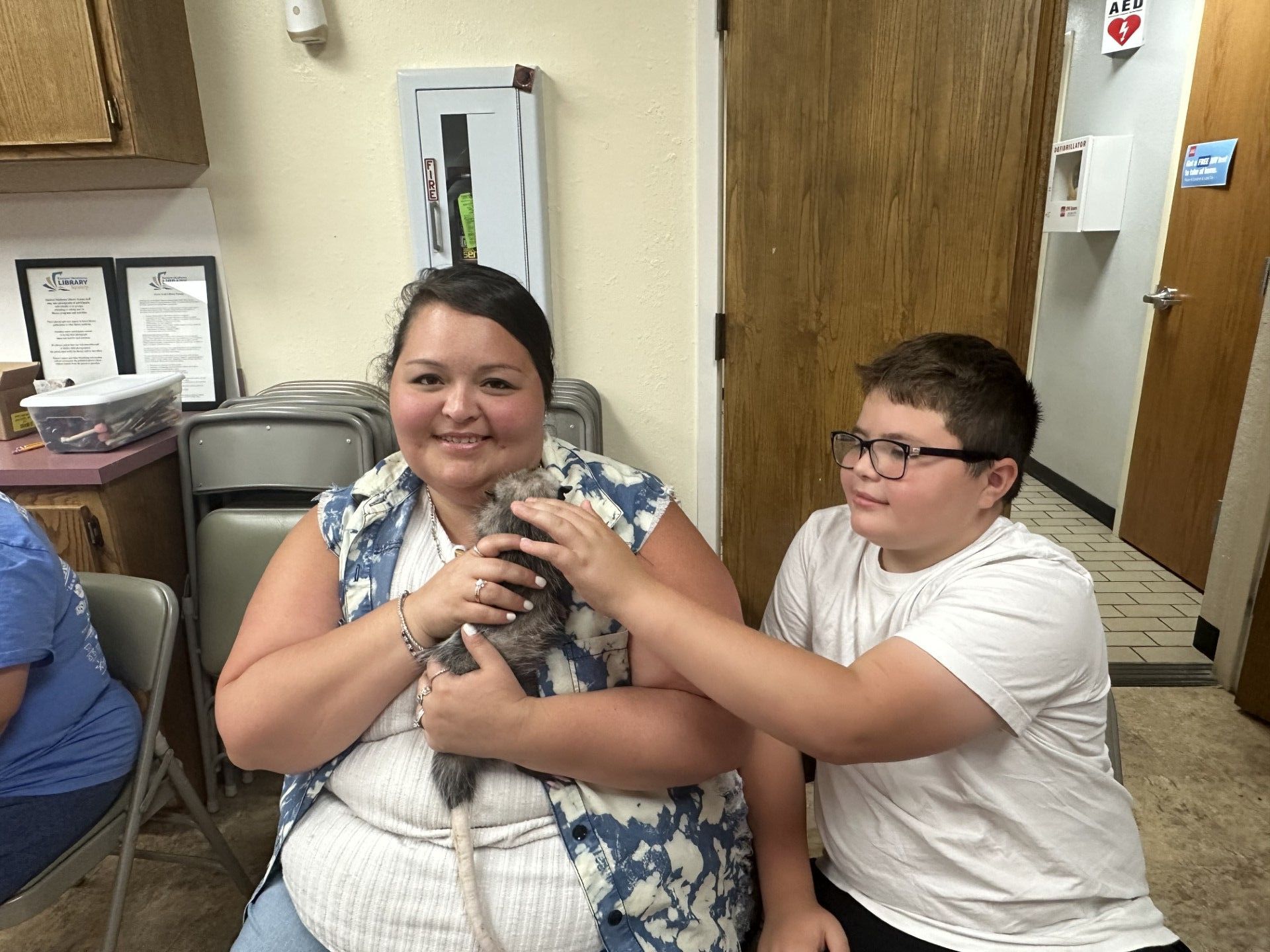 Woman and boy petting an opossum indoors.