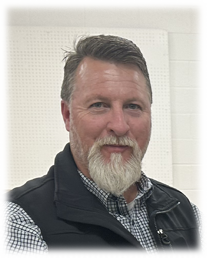 A man with a beard is wearing a black vest and a plaid shirt.