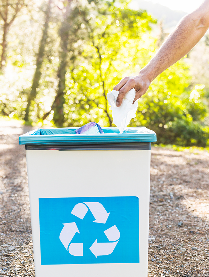 A person is throwing a piece of paper into a recycling bin.