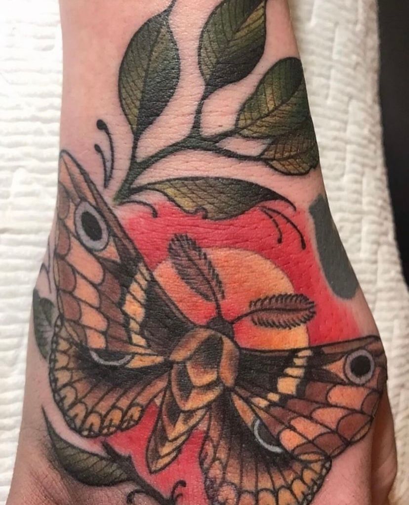 a person has a tattoo of a moth and leaves on their wrist