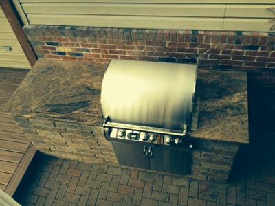 A grill is built into a brick wall with a granite counter top.
