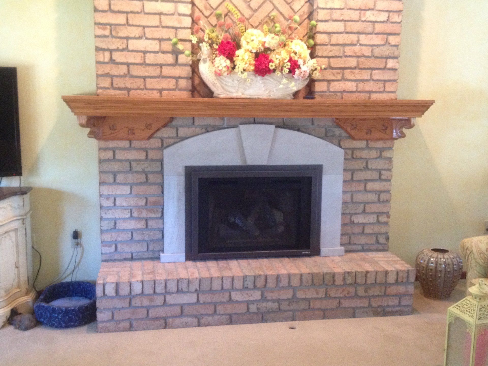 A brick fireplace in a living room with flowers on the mantle