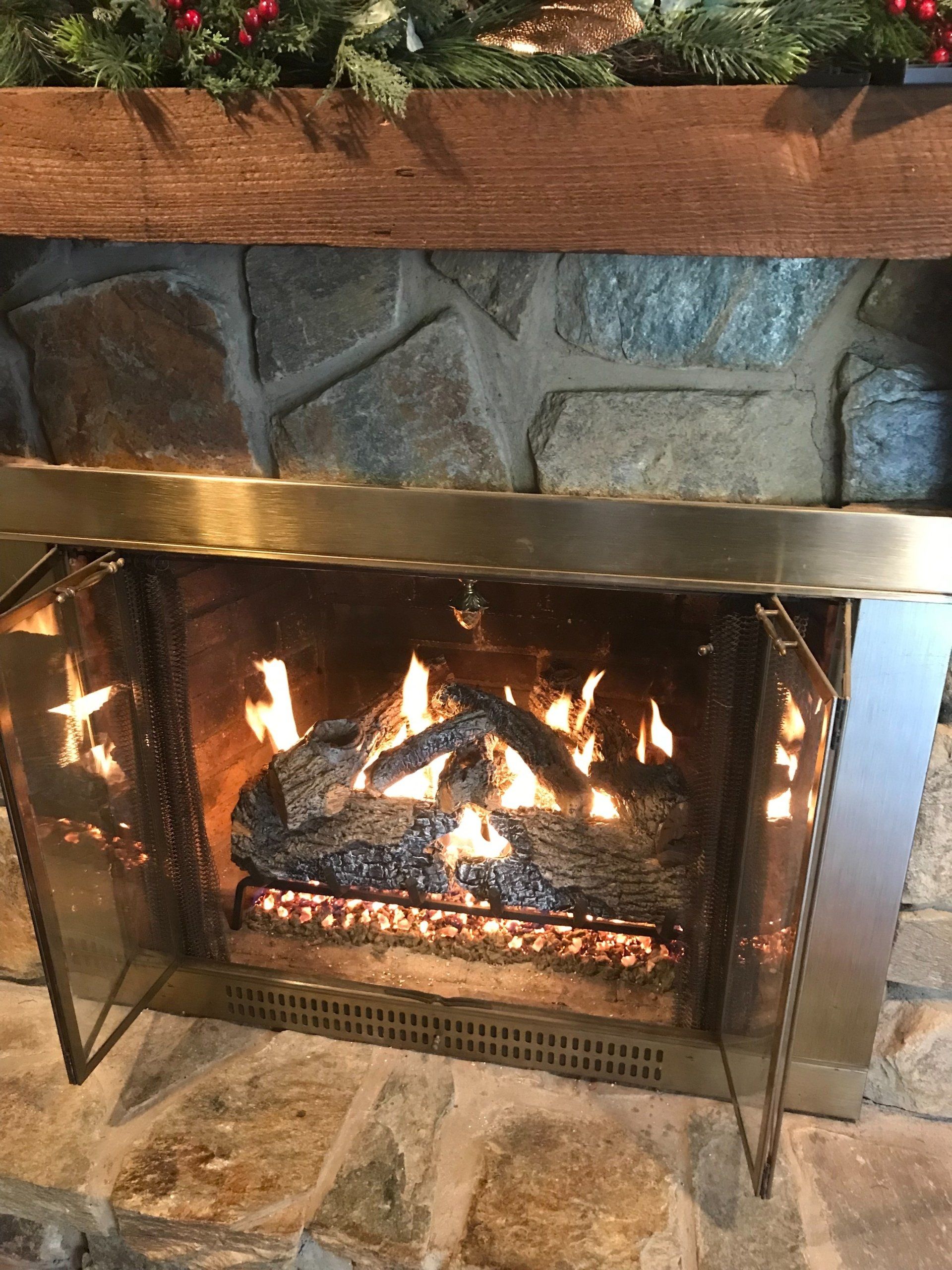 A fireplace with the doors open and a christmas tree in the background.