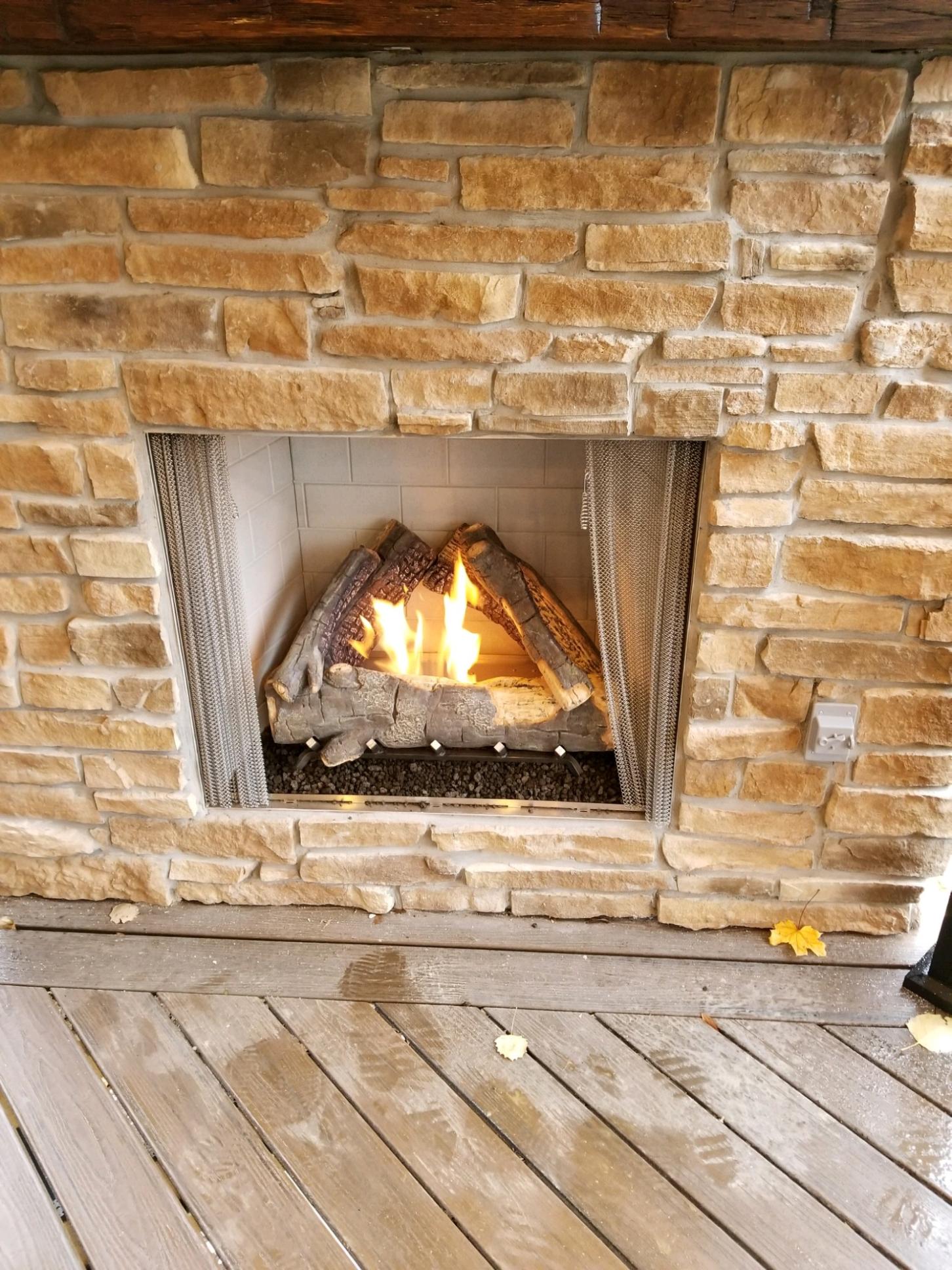 A lit gas fireplace with faux logs in a stone surround.