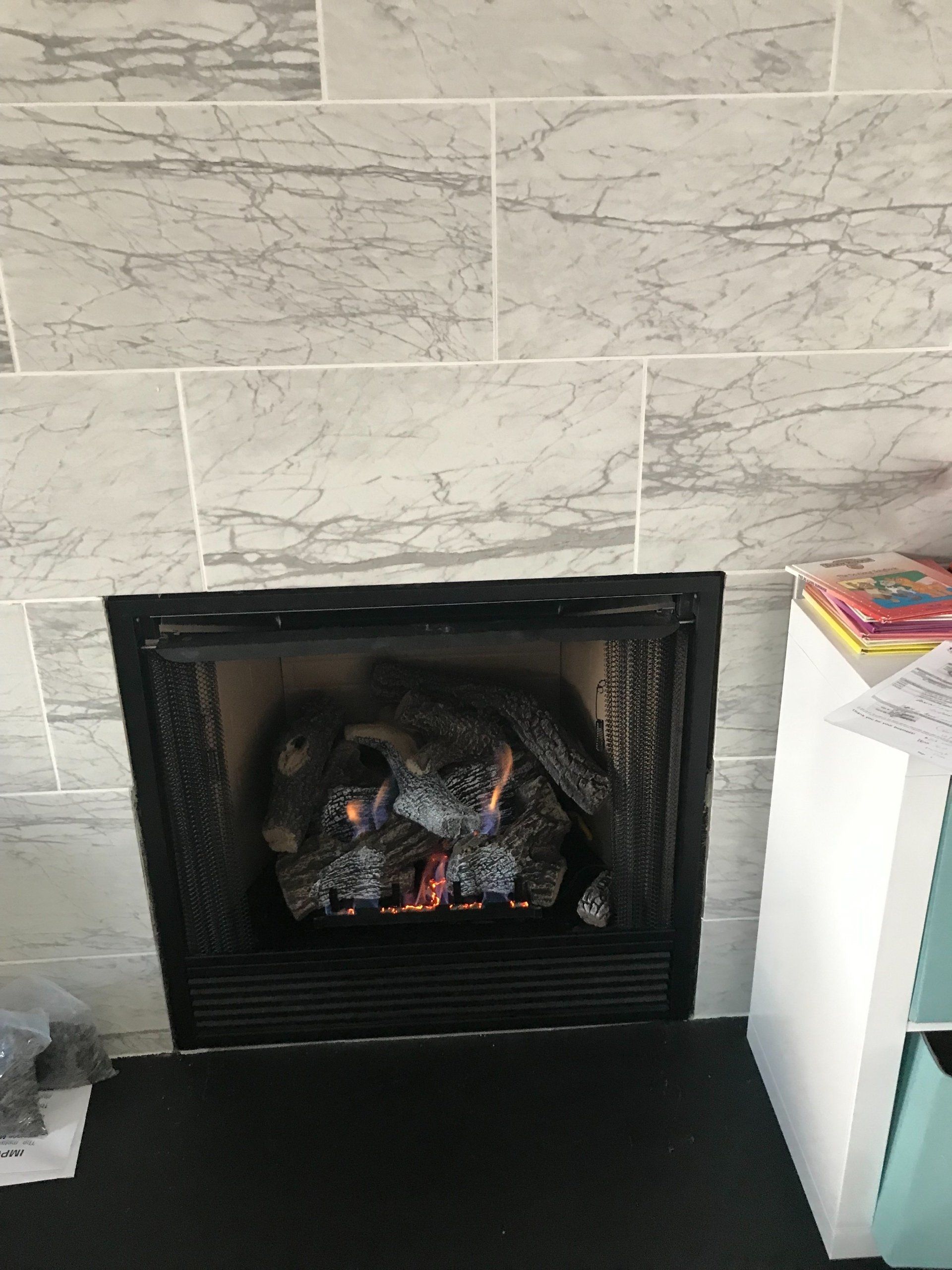 A fireplace with a marble wall and a stack of books on a shelf.