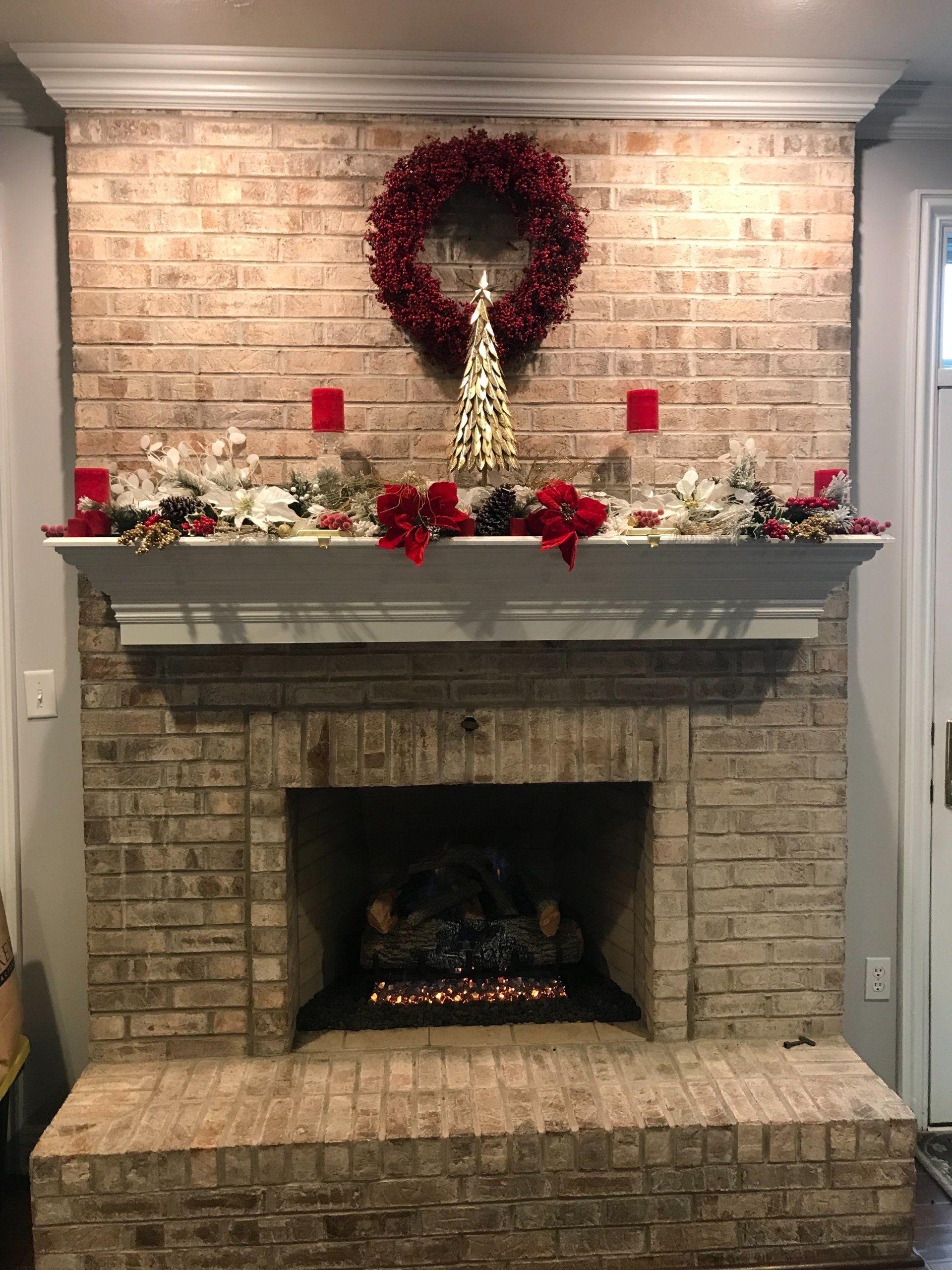 A brick fireplace decorated for christmas with a wreath and candles.