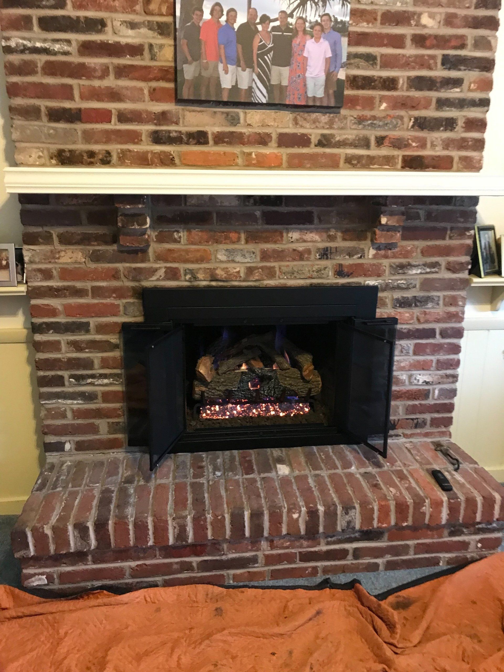A brick fireplace with a picture of a family on the mantle.