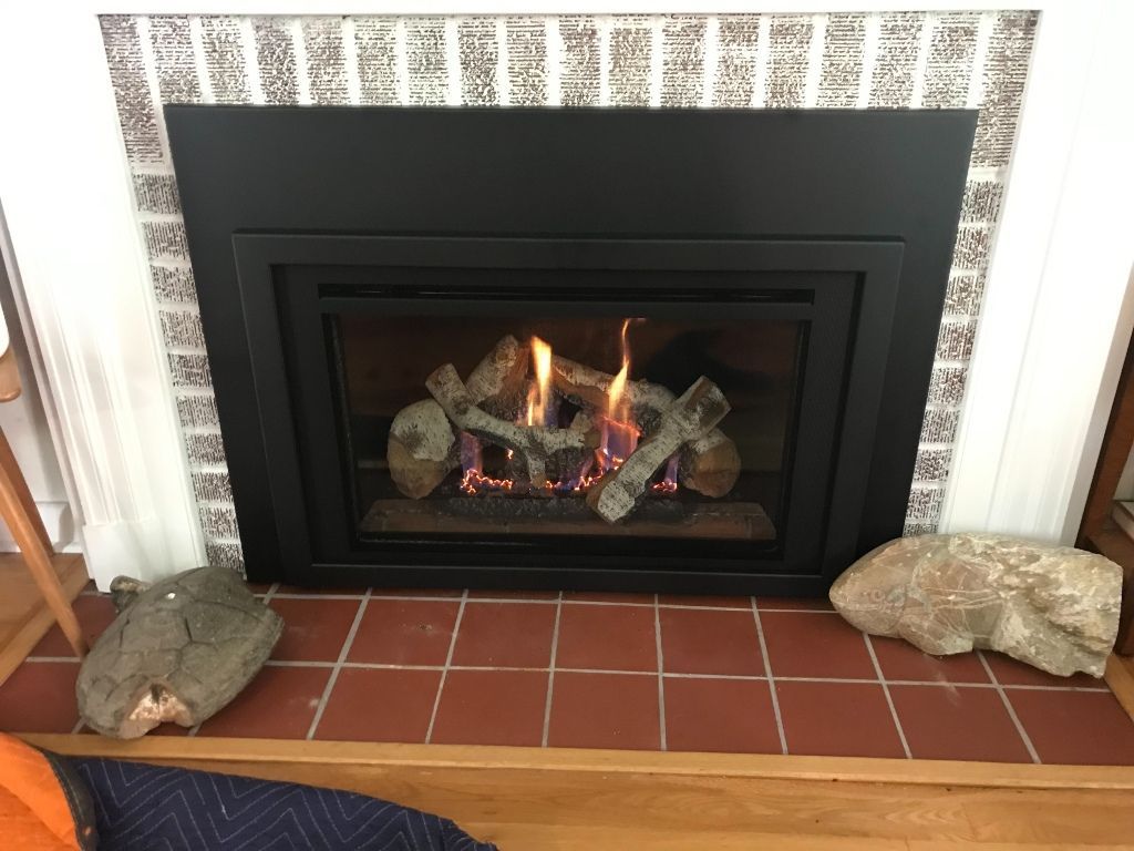 A fireplace with logs in it is sitting on a tiled floor in a living room.