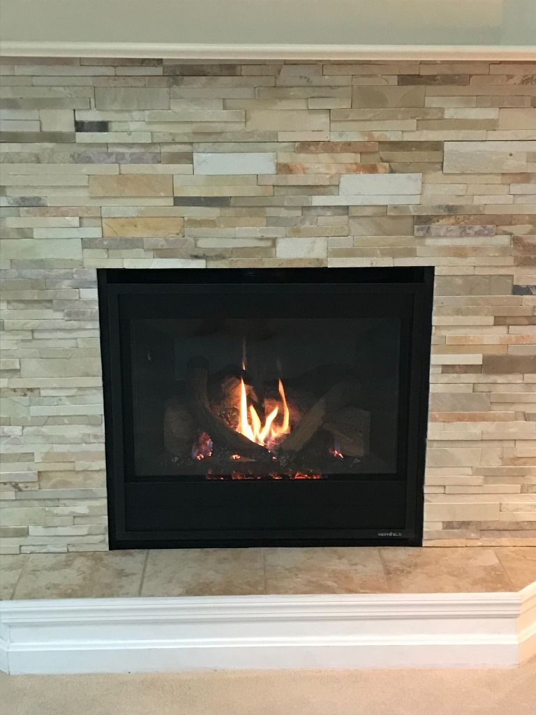 Fireplace with flames inside, surrounded by stone and a black frame. White trim below.