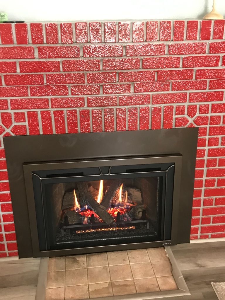 A gas fireplace is sitting in front of a red brick wall.