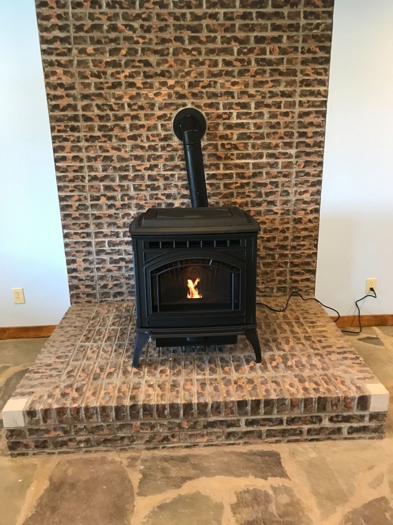 A wood stove is sitting in front of a brick fireplace.
